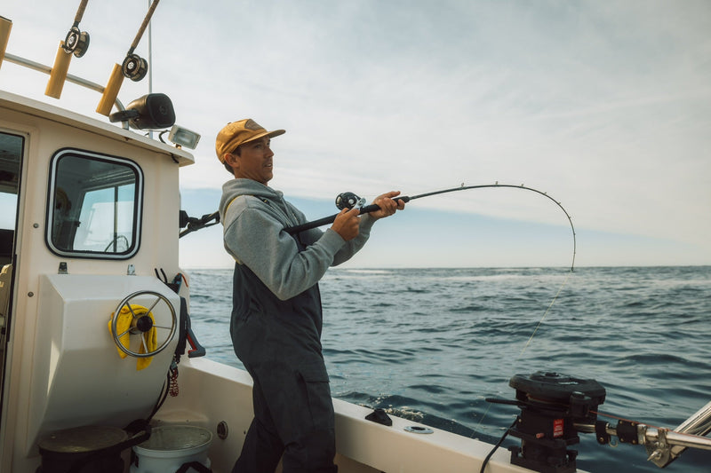 Brody Pigeau in Taku waterproof bibs landing a big fish on his boat