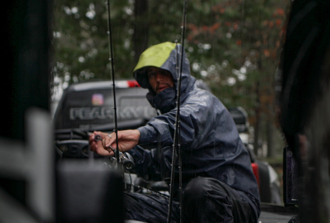 Angler Carl Jocumsen prepares his fishing rods while wearing heavy rain gear during a downpour.