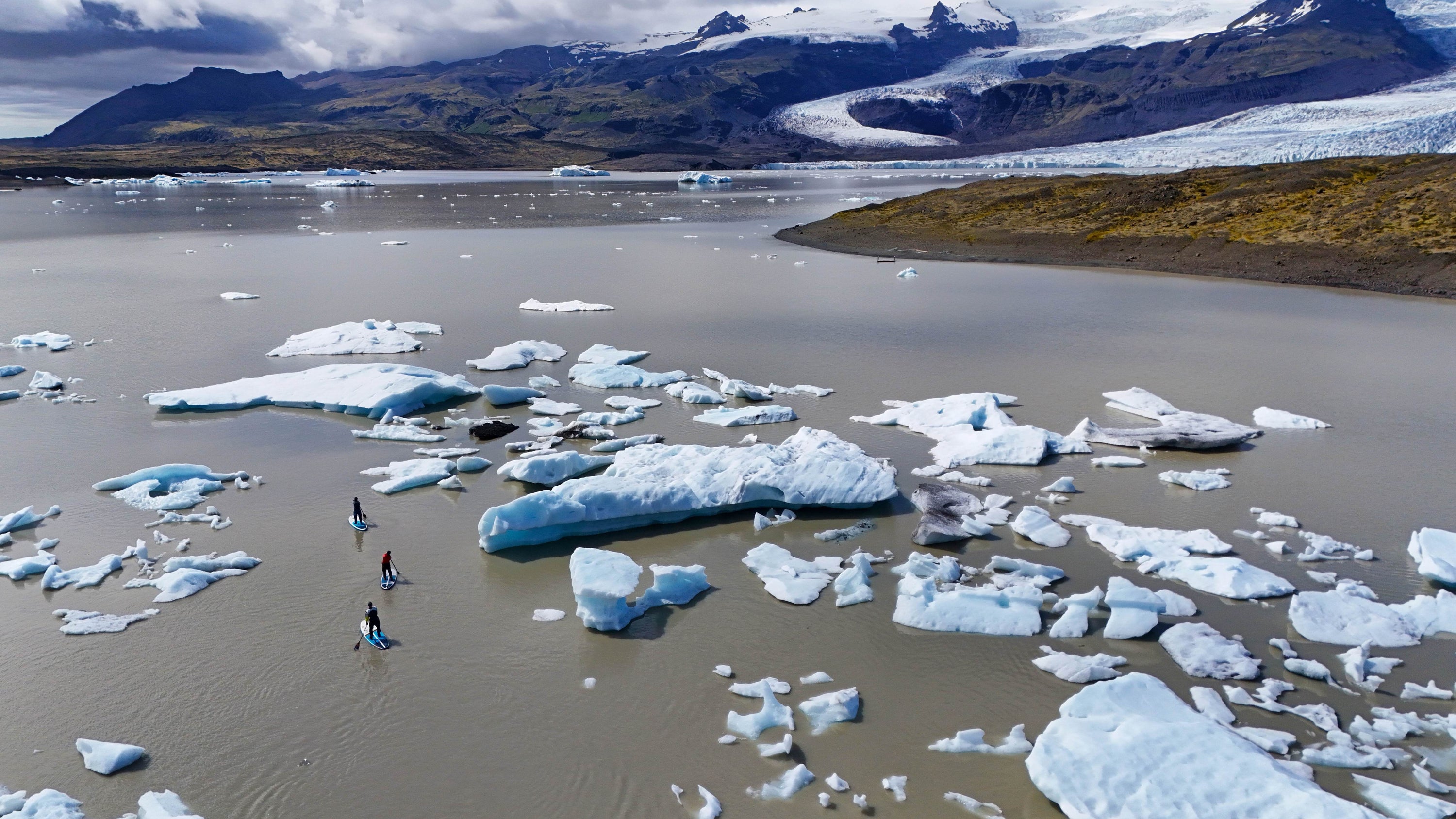 An aerial view of three paddlers in Mustang Survival drysuits navigating paddleboards through icebergs in Iceland.