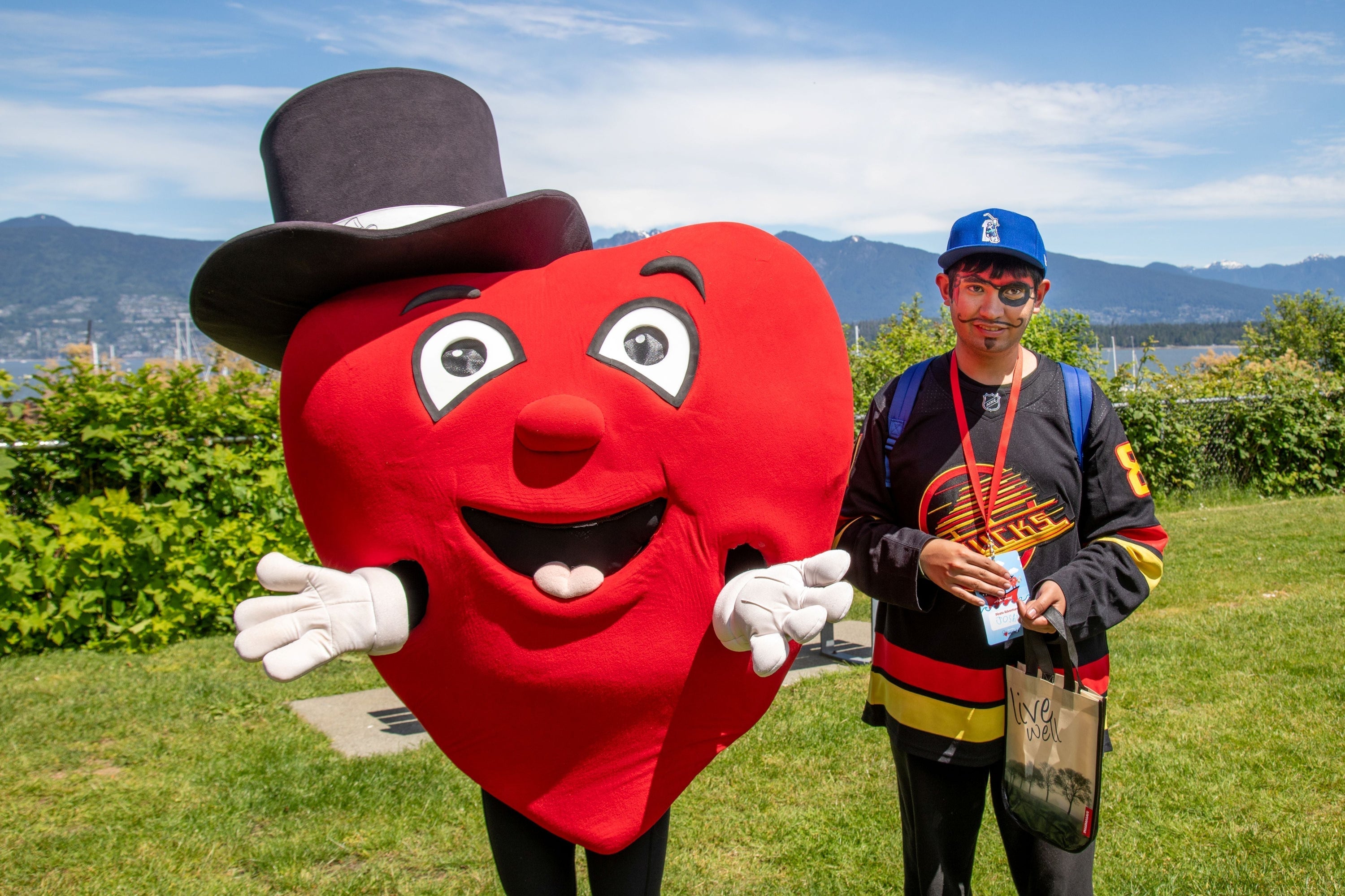 The Variety Children's Charity heart mascot poses with a participant at a grassy waterfront park during Boat for Hope.