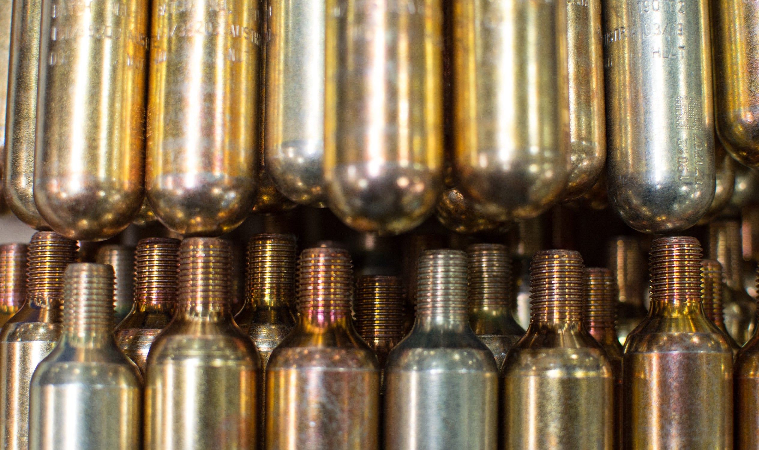 Rows of brass-colored, threaded CO2 cylinders used for inflatable PFD re-arming and re-charging kits.