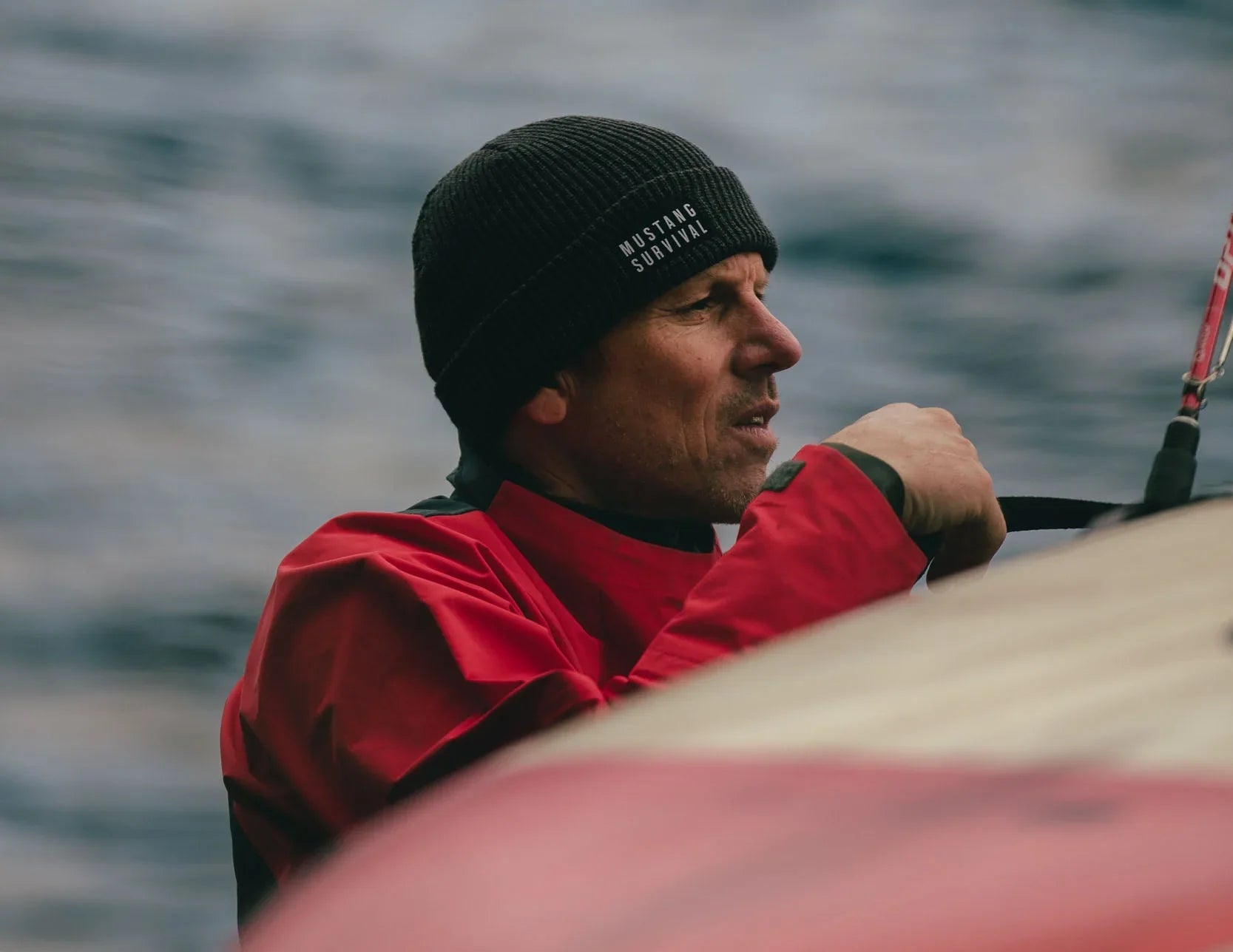 A professional paddler wearing a grey Mustang Survival beanie and a red Callan Waterproof Top straps down his SUP board.