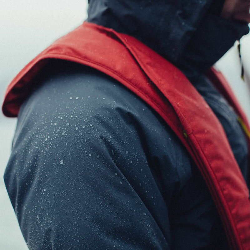 Boater wearing a red Mustang Survival MIT Inflatable PFD in the rain, showing the lightweight, low-profile fit designed for all-day comfort.