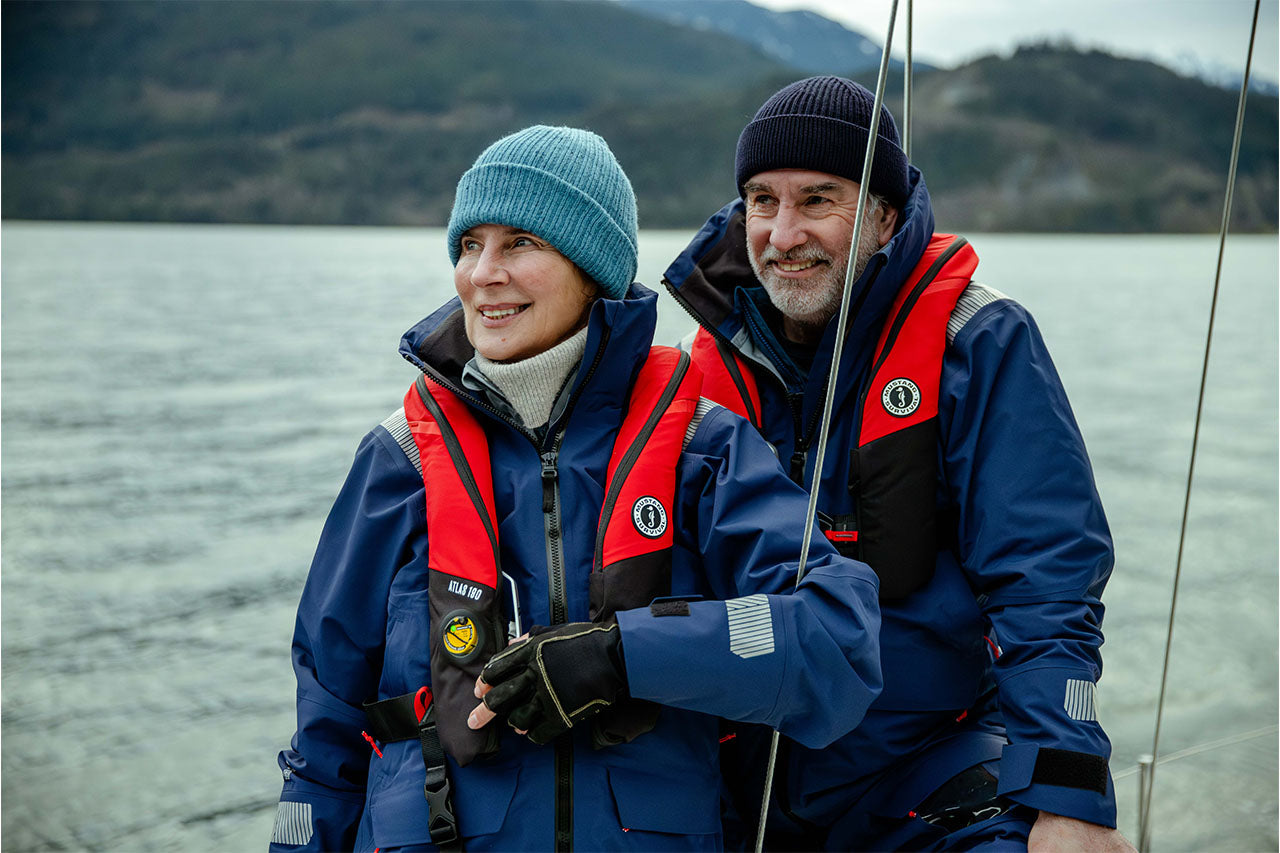 older man and woman on a winter day coastal sailing wearing proper gear and life jackets