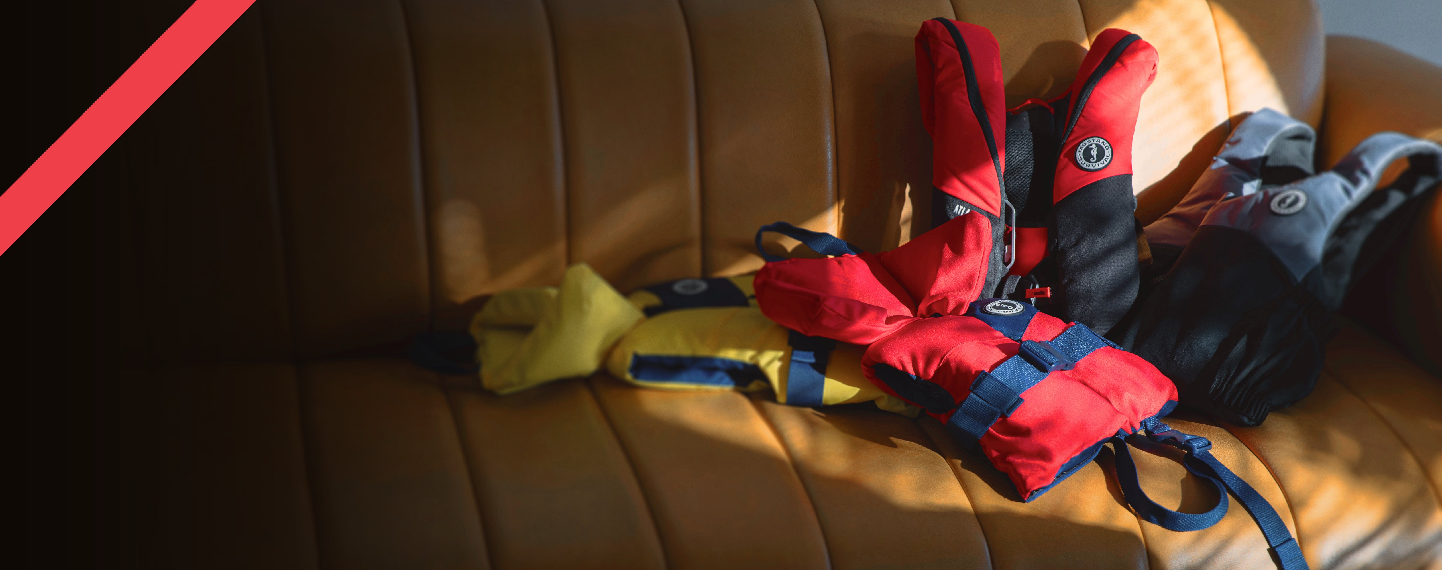 Mustang Survival PFDs and gear laid out for Holiday Gift Guide 2025 on a couch, featuring gifts for sailors, anglers, paddlers, and boaters.